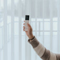 A hand holding the Novo remote in front of a sunlit window
