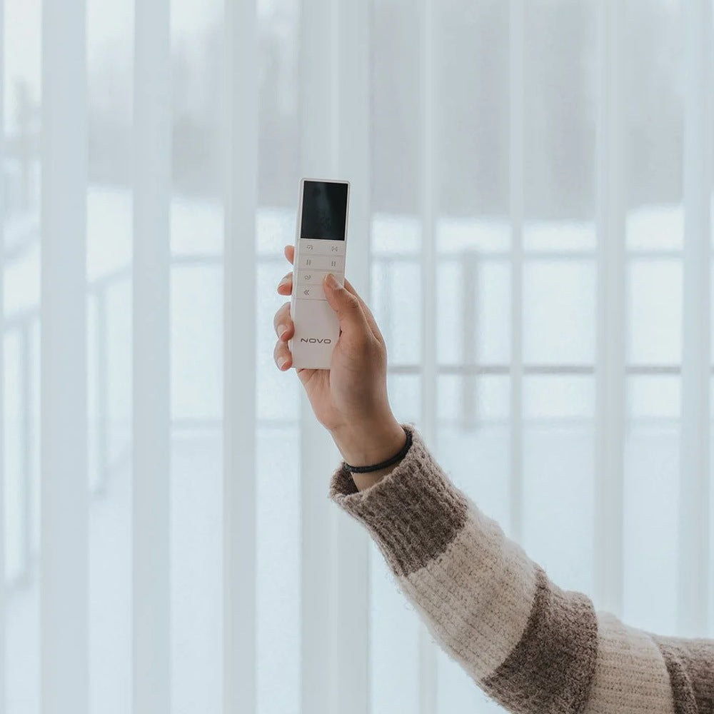 A hand holding the Novo remote in front of a sunlit window