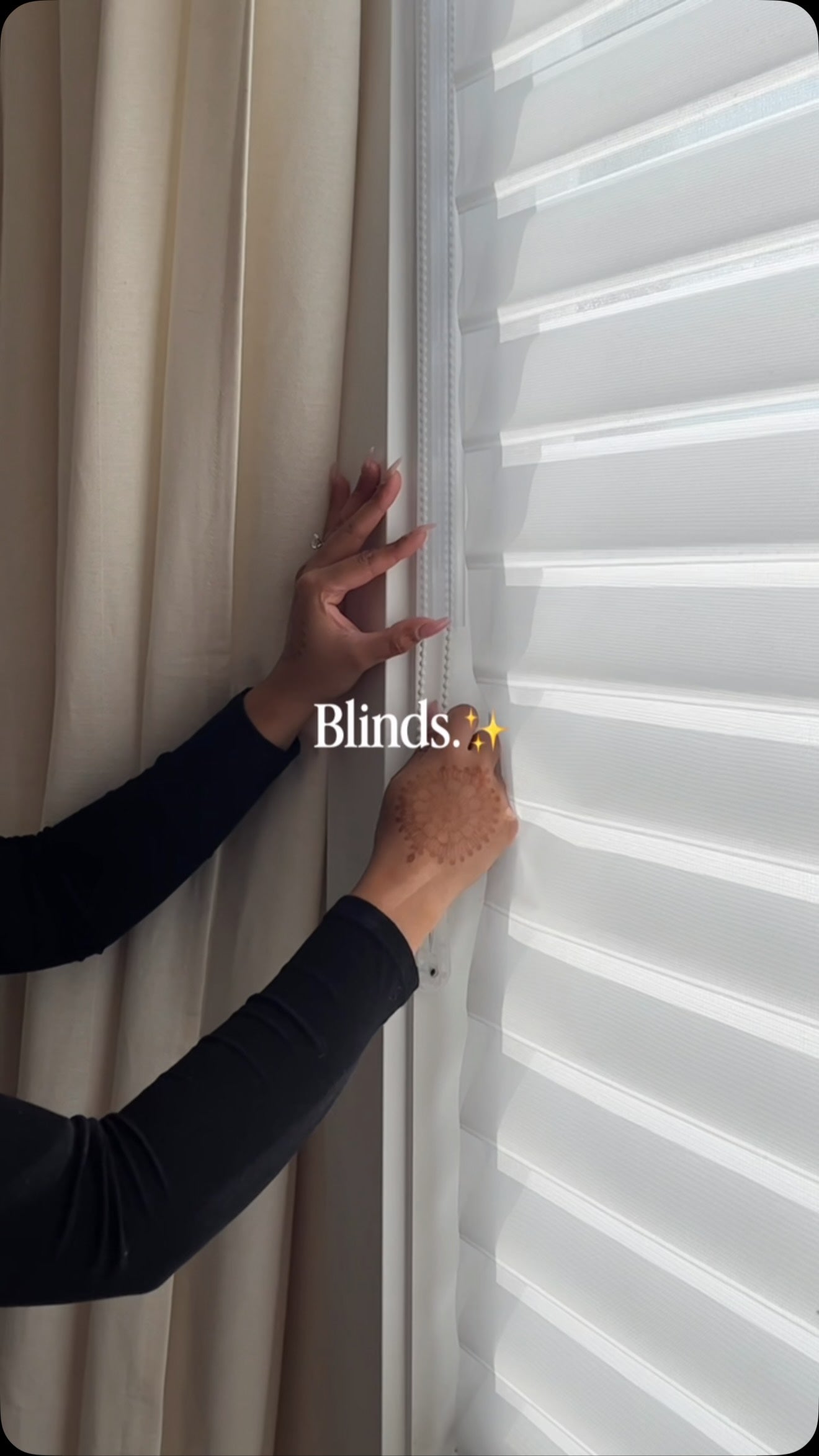 Hands operating a sheer window shade beside a window.